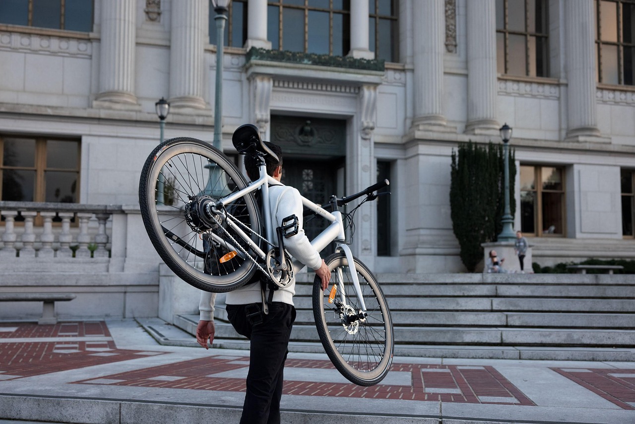 Person trägt ein Fahrrad vor einem großen historischen Gebäude mit Säulen.