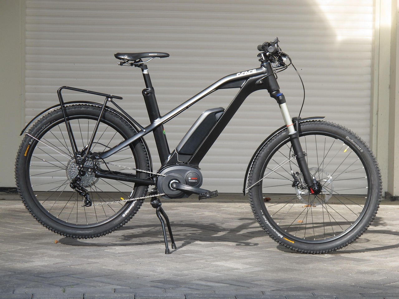 Schwarzes E-Bike mit dickem Rahmen vor Garage auf Pflastersteinen.