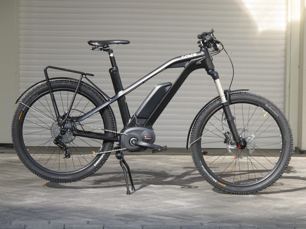Schwarzes E-Bike mit dickem Rahmen vor Garage auf Pflastersteinen.