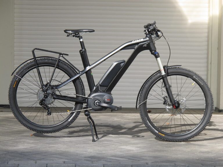Schwarzes E-Bike mit dickem Rahmen vor Garage auf Pflastersteinen.